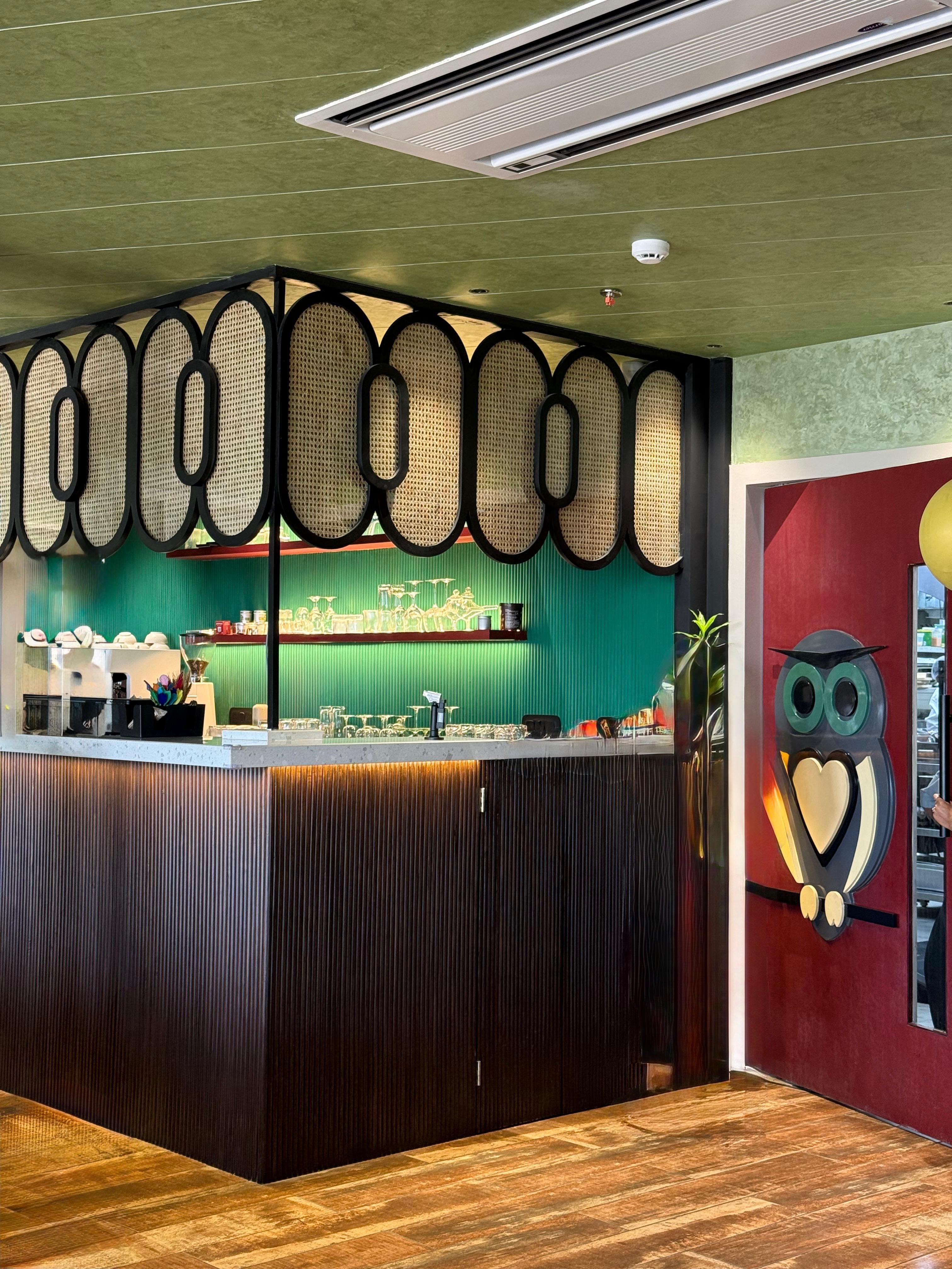 Coffee bar with a teal ribbed wall, woven oval screen, and dark wood counter.